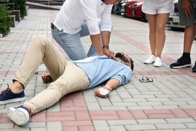 Photo of Passerby performing CPR on unconscious young man outdoors. First aid