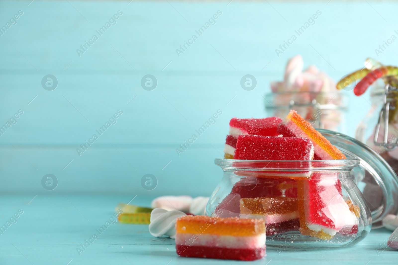 Photo of Jar with delicious colorful jelly candies on light blue wooden table, closeup. Space for text