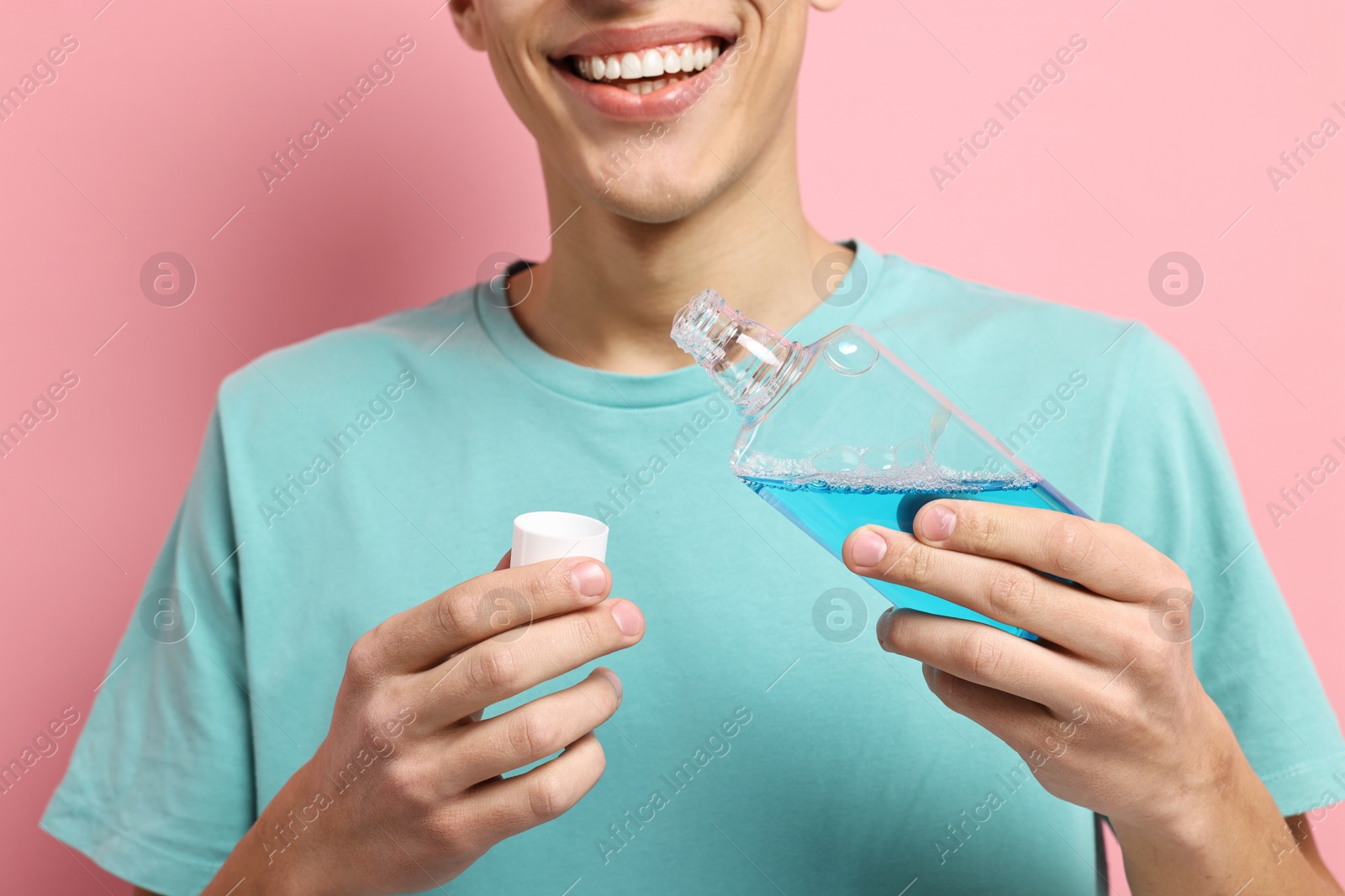 Photo of Young man using mouthwash on pink background, closeup