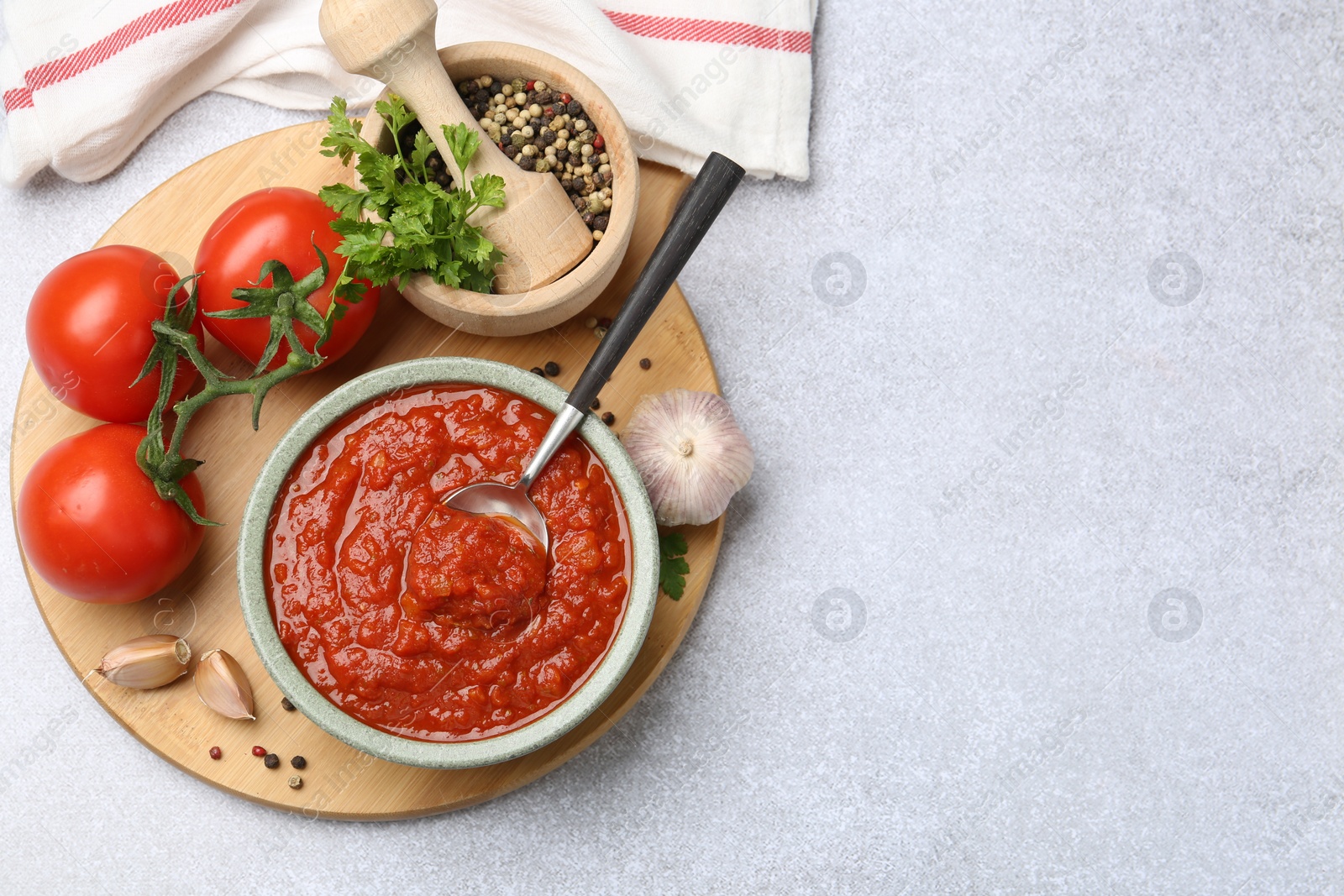 Photo of Homemade tomato sauce in bowl, spoon and fresh ingredients on light grey table, flat lay. Space for text