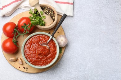 Photo of Homemade tomato sauce in bowl, spoon and fresh ingredients on light grey table, flat lay. Space for text