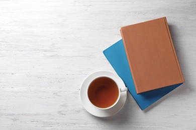 Hardcover books and cup of tea on white wooden table, flat lay. Space for text