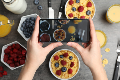 Blogger taking photo of oatmeal with berries at grey table, closeup