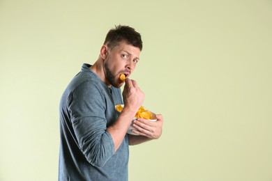 Greedy man hiding bowl with chips on light background, space for text