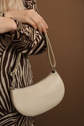 Photo of Woman with stylish baguette handbag on brown background, closeup