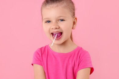Photo of Cute little girl eating lollipop on pink background