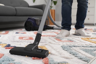 Man cleaning carpet with vacuum cleaner at home, closeup. Space for text