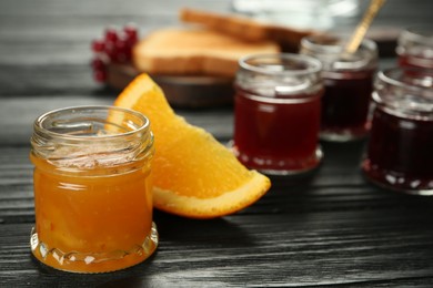 Photo of Jar of sweet orange jam on black wooden table, space for text