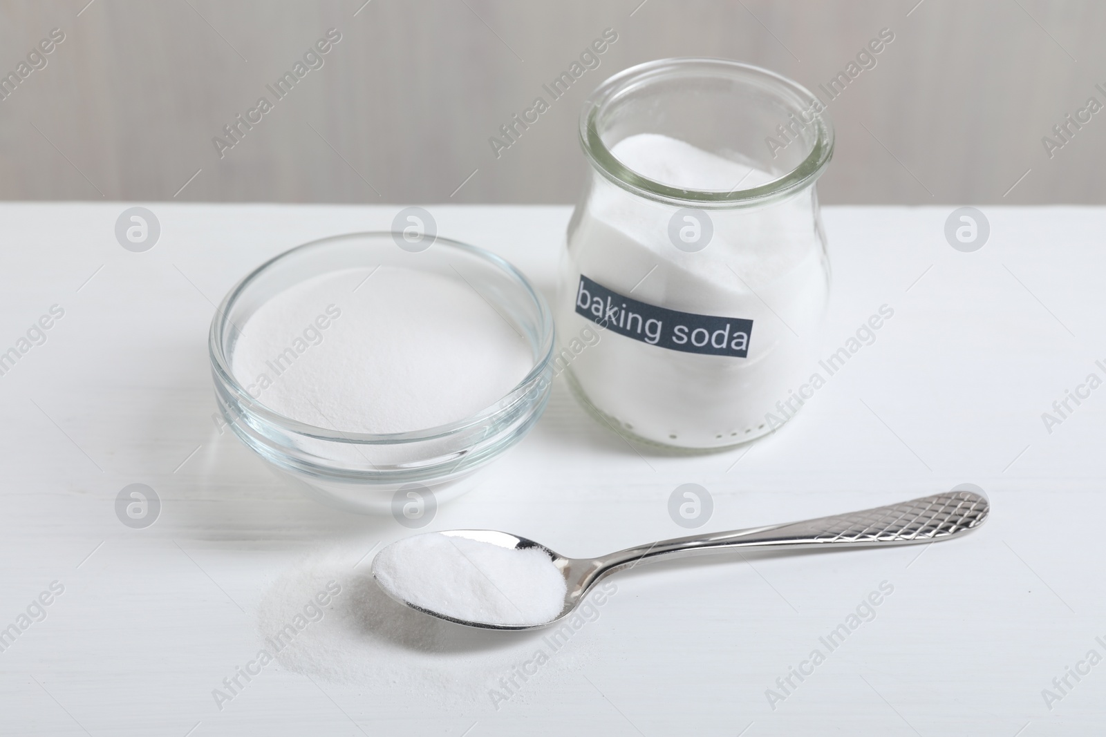 Photo of Baking soda in bowl, glass jar and spoon on white wooden table