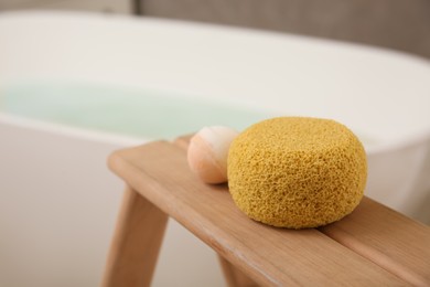 Sponge and bath bomb on wooden stand near tub indoors