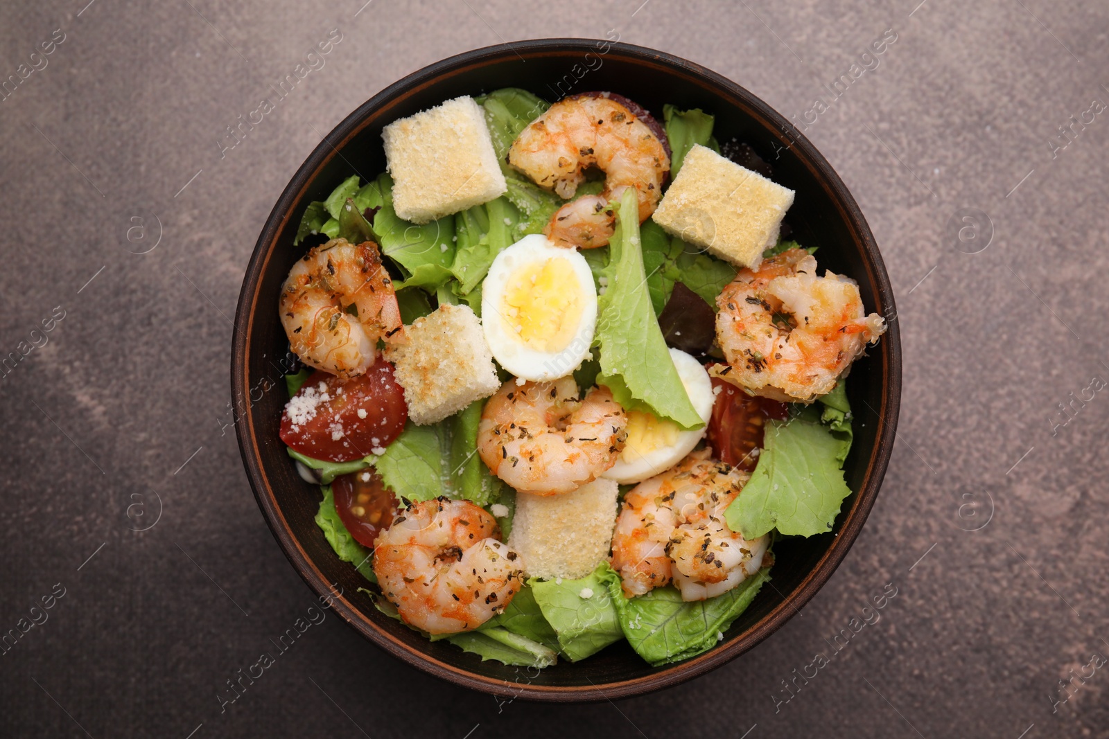 Photo of Delicious Caesar salad with shrimps on brown table, top view