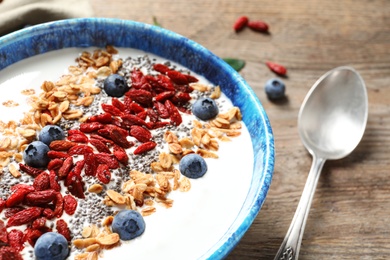 Photo of Smoothie bowl with goji berries and spoon on wooden table, closeup