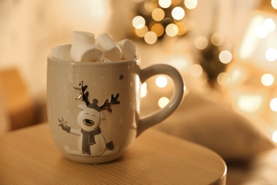 Cup of hot drink with marshmallows on small wooden table, space for text. Christmas atmosphere