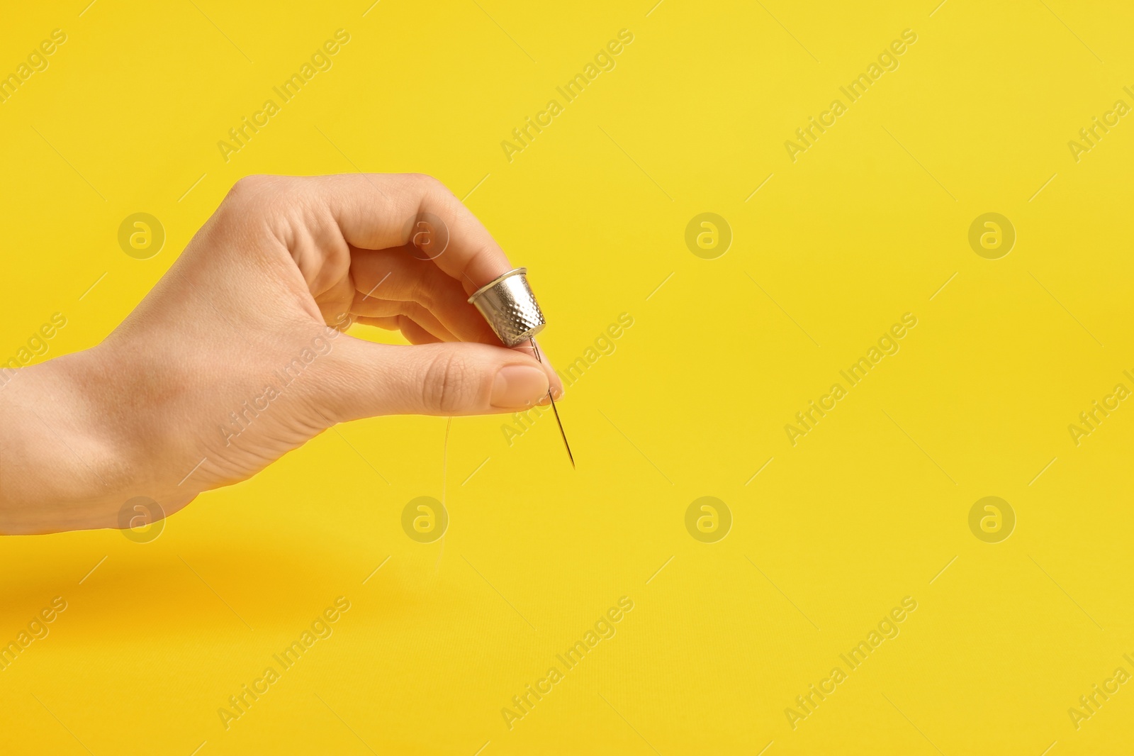 Photo of Woman with thimble, thread and sewing needle on yellow background, closeup. Space for text