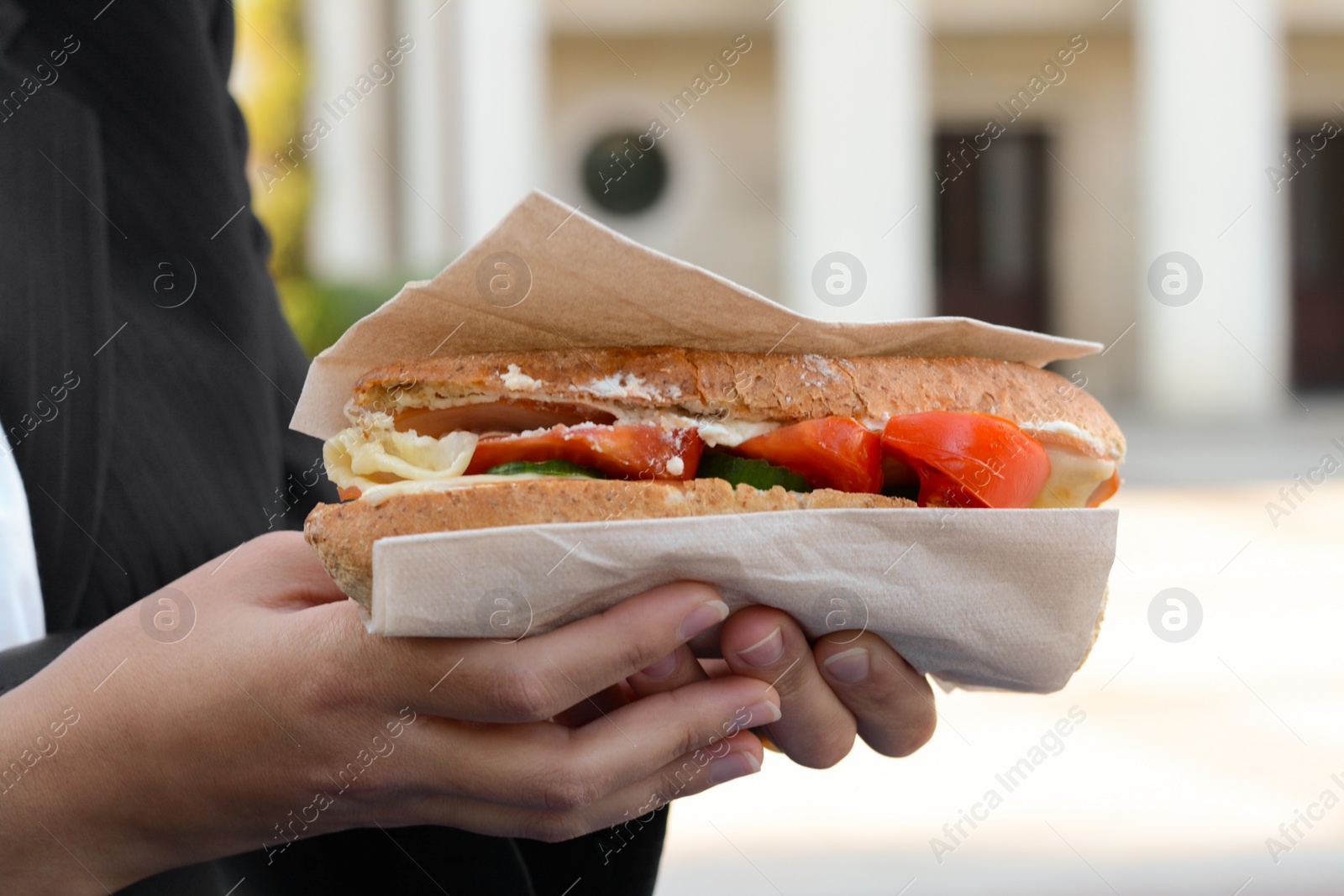 Photo of Woman holding tasty sandwich with vegetables outdoors, closeup. Street food