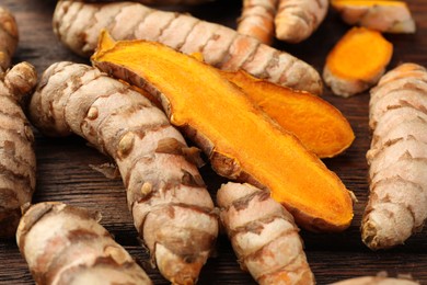 Photo of Many fresh turmeric roots on wooden table, closeup