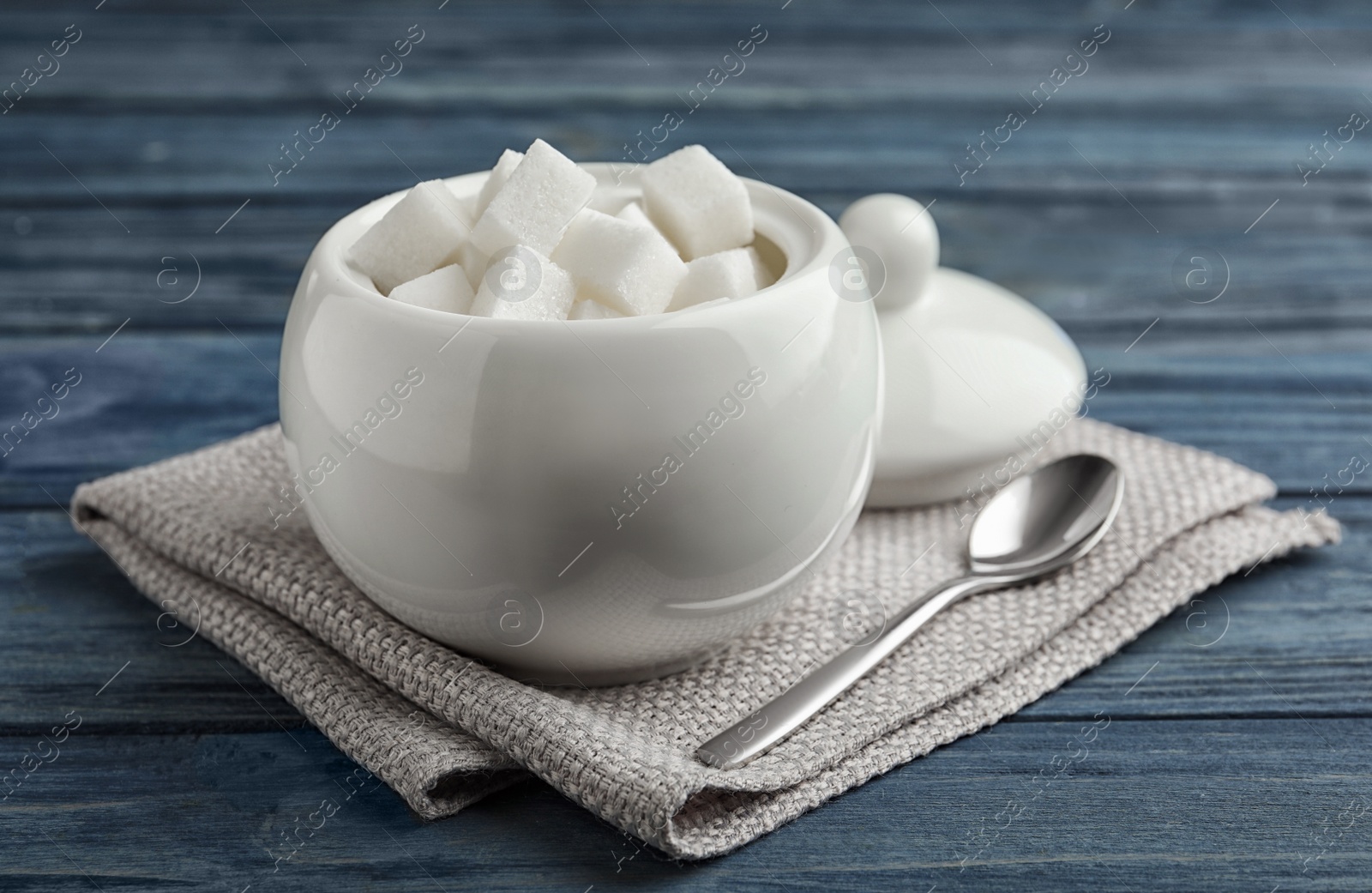 Photo of Refined sugar cubes in ceramic bowl on blue wooden table