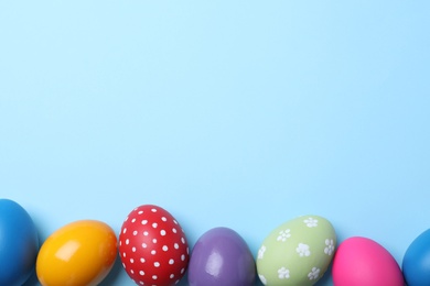 Photo of Bright painted eggs on light blue background, flat lay with space for text. Happy Easter