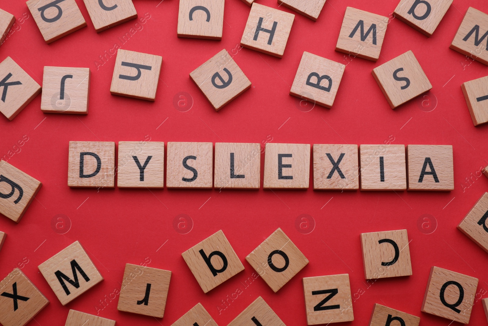 Photo of Wooden tiles with word Dyslexia on red background, flat lay