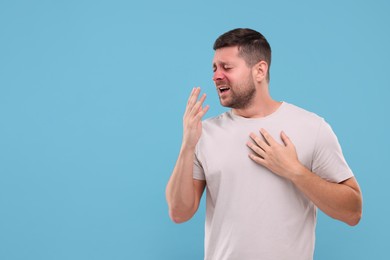 Photo of Allergy symptom. Man sneezing on light blue background. Space for text