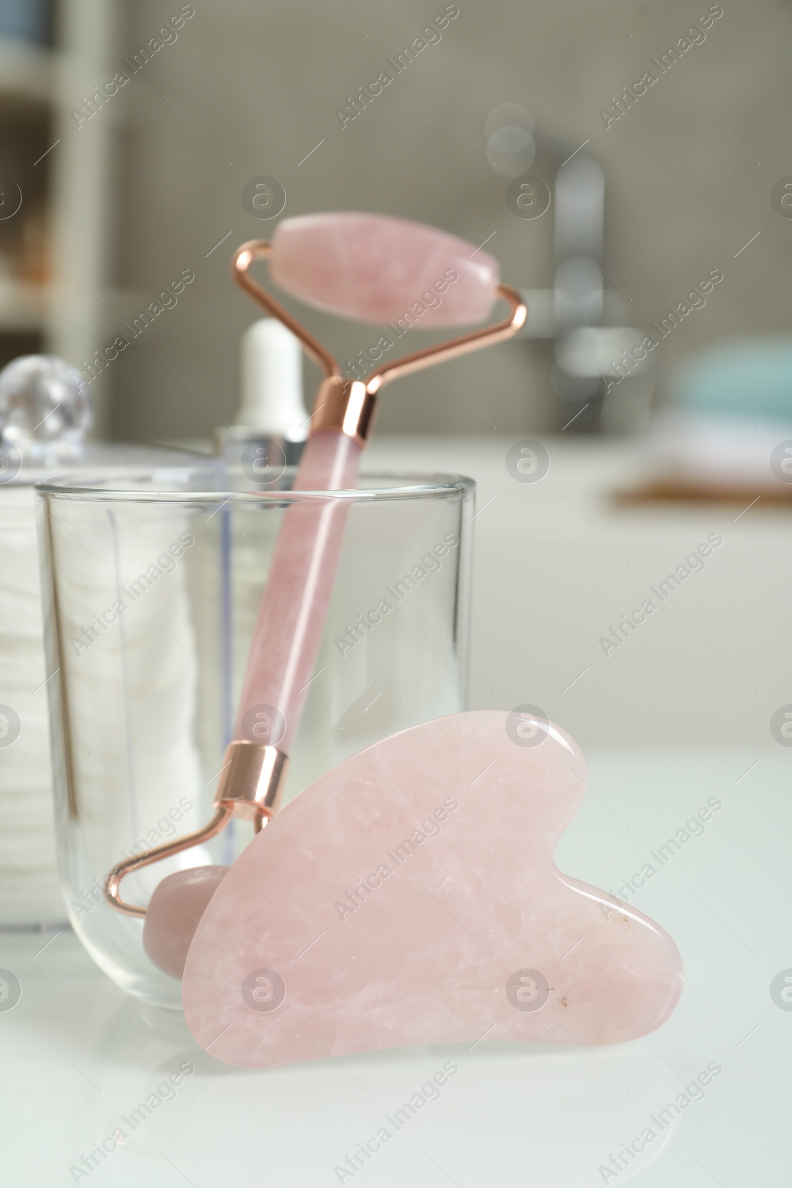 Photo of Rose quartz gua sha tool, natural face roller and toiletries on white table indoors