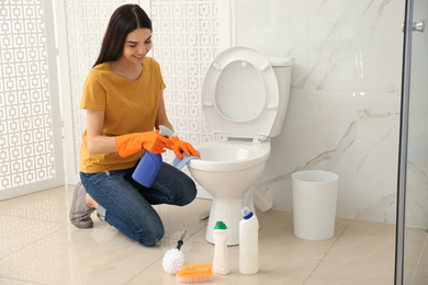 Young woman cleaning toilet bowl in bathroom