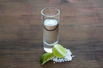 Photo of Mexican tequila shot with lime slices and salt on wooden table. Drink made from agave