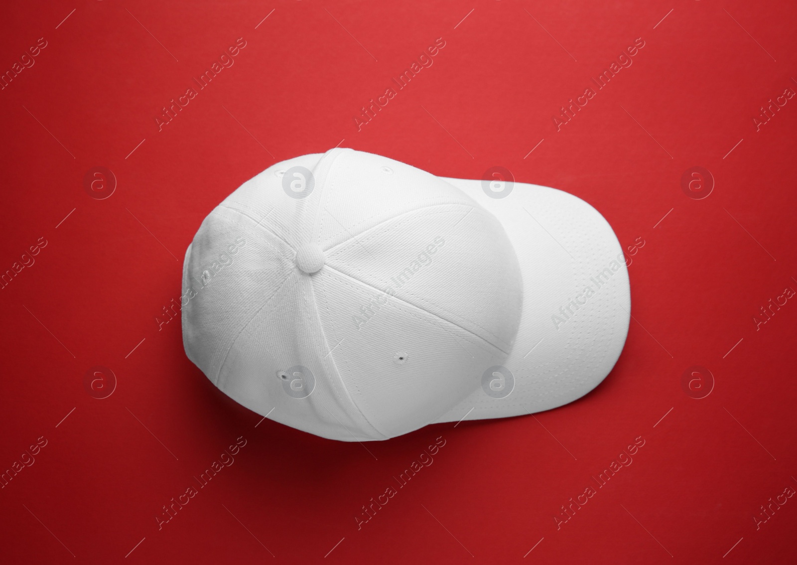 Photo of Stylish white baseball cap on red background, top view