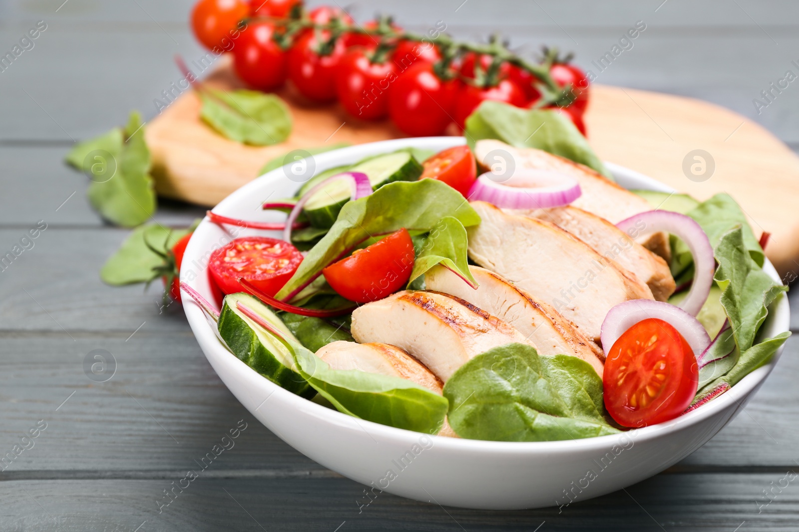 Photo of Delicious salad with chicken and vegetables on grey wooden table, closeup