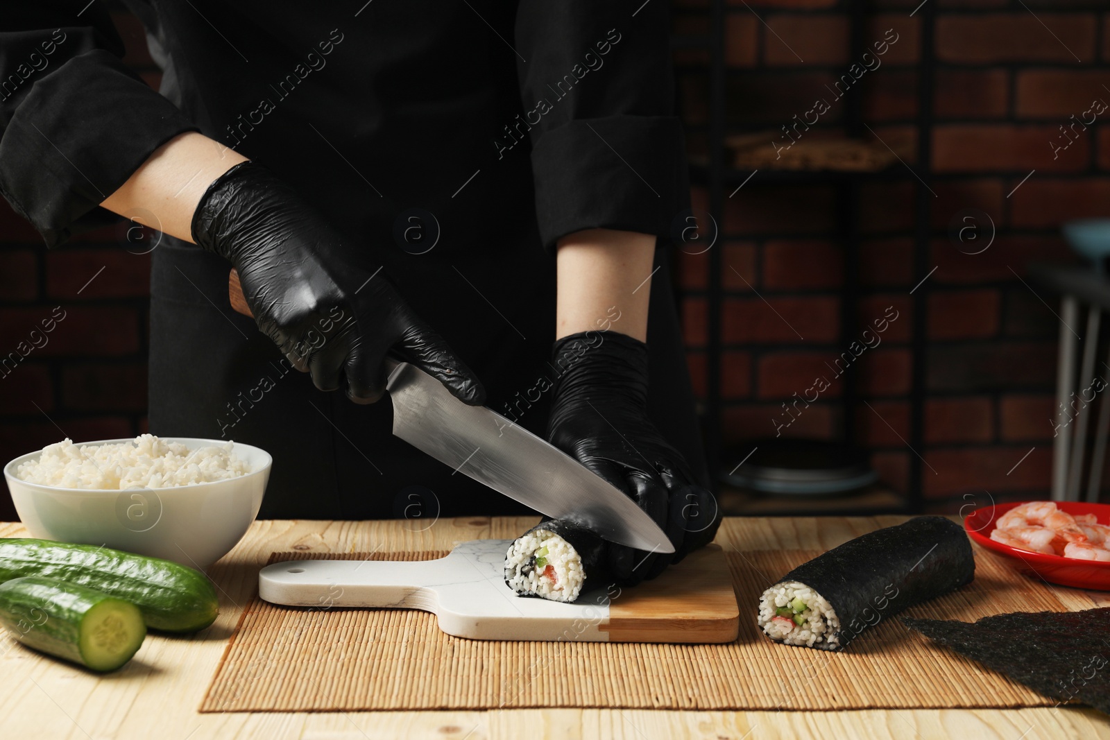 Photo of Chef in gloves cutting sushi roll at wooden table, closeup