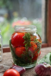 Glass jar with vegetables, herbs and brine on wooden table indoors