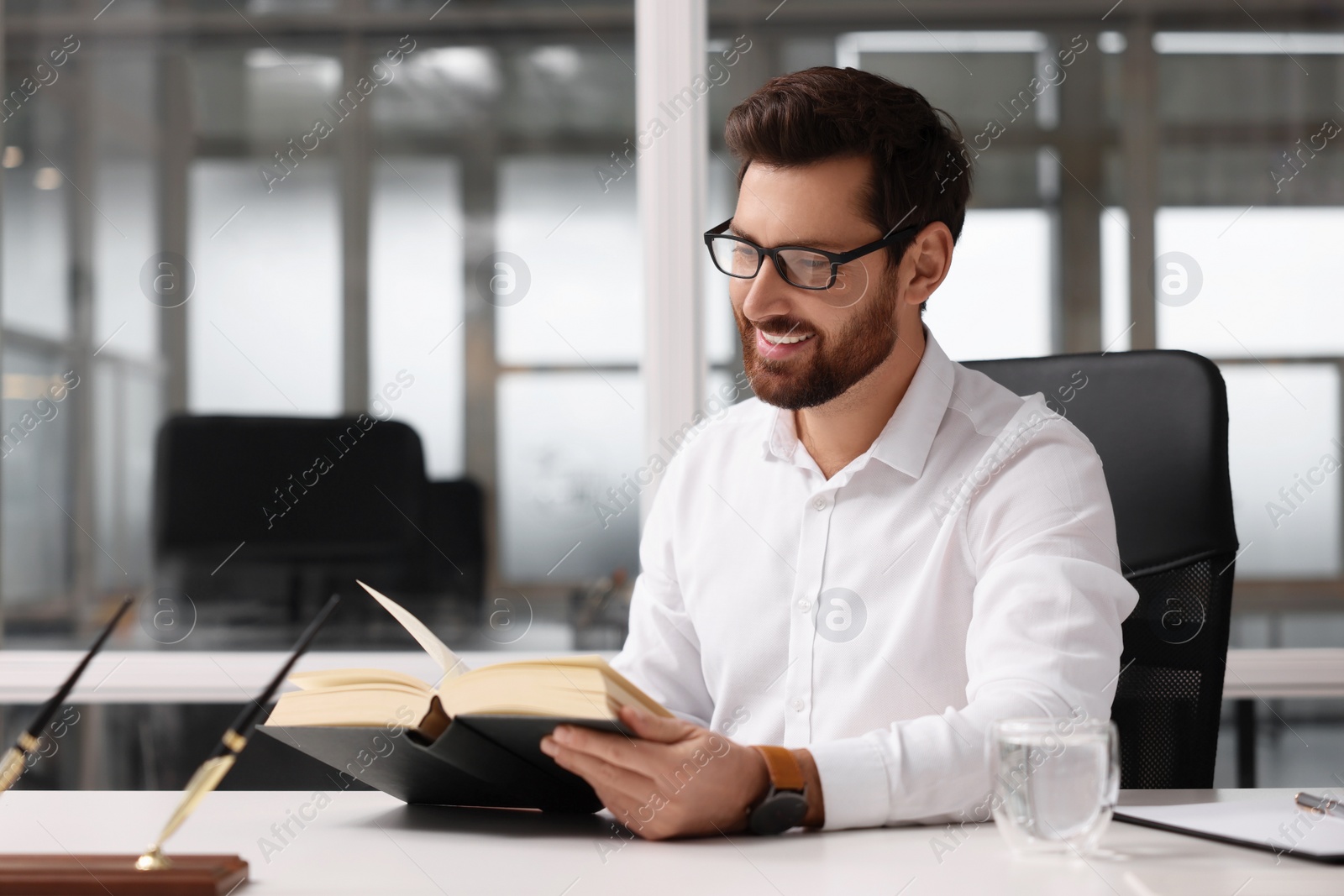 Photo of Smiling man reading book at table in office, space for text. Lawyer, businessman, accountant or manager