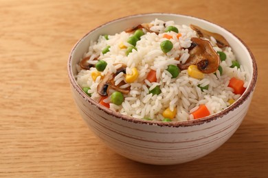 Bowl of delicious rice with vegetables on wooden table, closeup