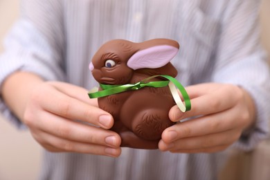 Photo of Woman with chocolate Easter bunny on beige background, closeup
