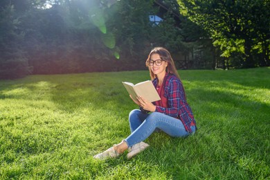 Young woman reading book in park on sunny day