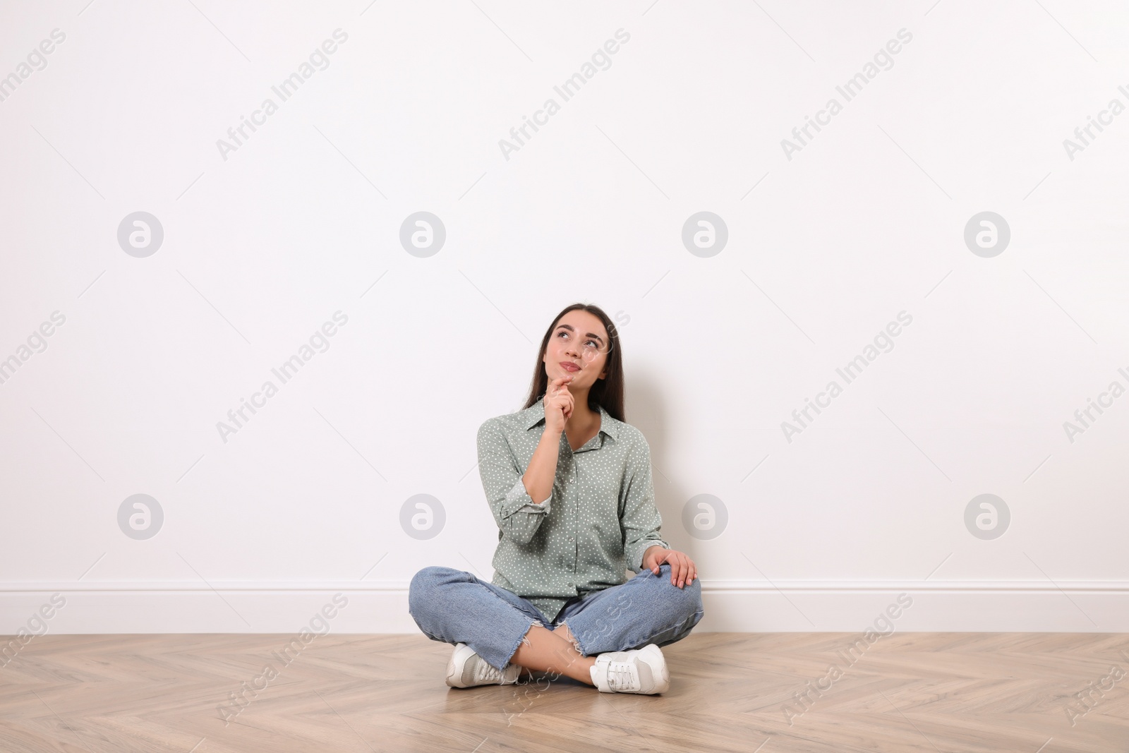 Photo of Young woman sitting on floor near white wall indoors