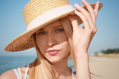 Beautiful young woman with straw hat near sea on sunny day in summer, closeup