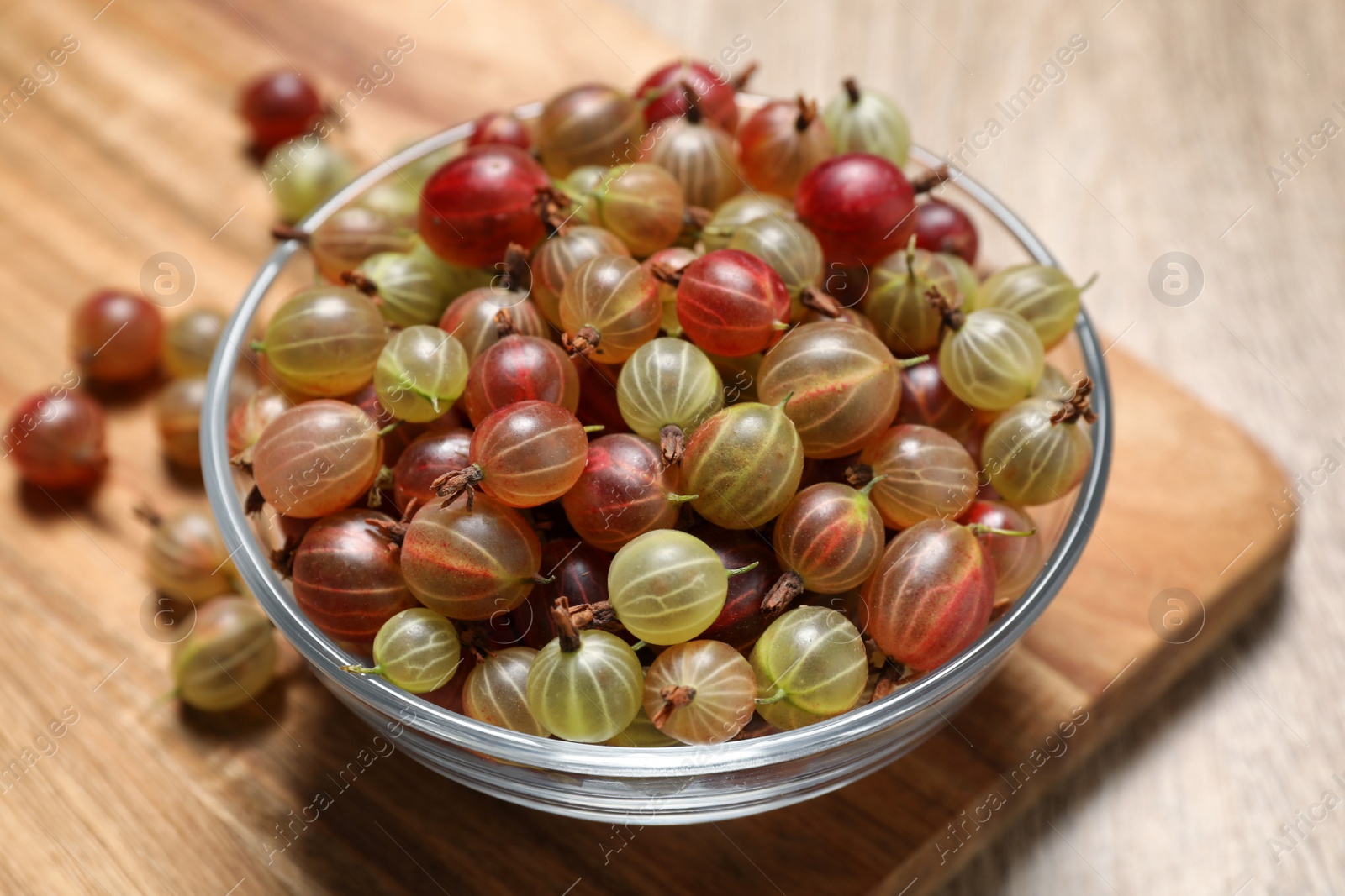 Photo of Glass bowl with fresh ripe gooseberries on wooden table, closeup