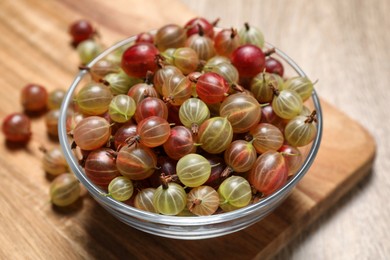 Glass bowl with fresh ripe gooseberries on wooden table, closeup