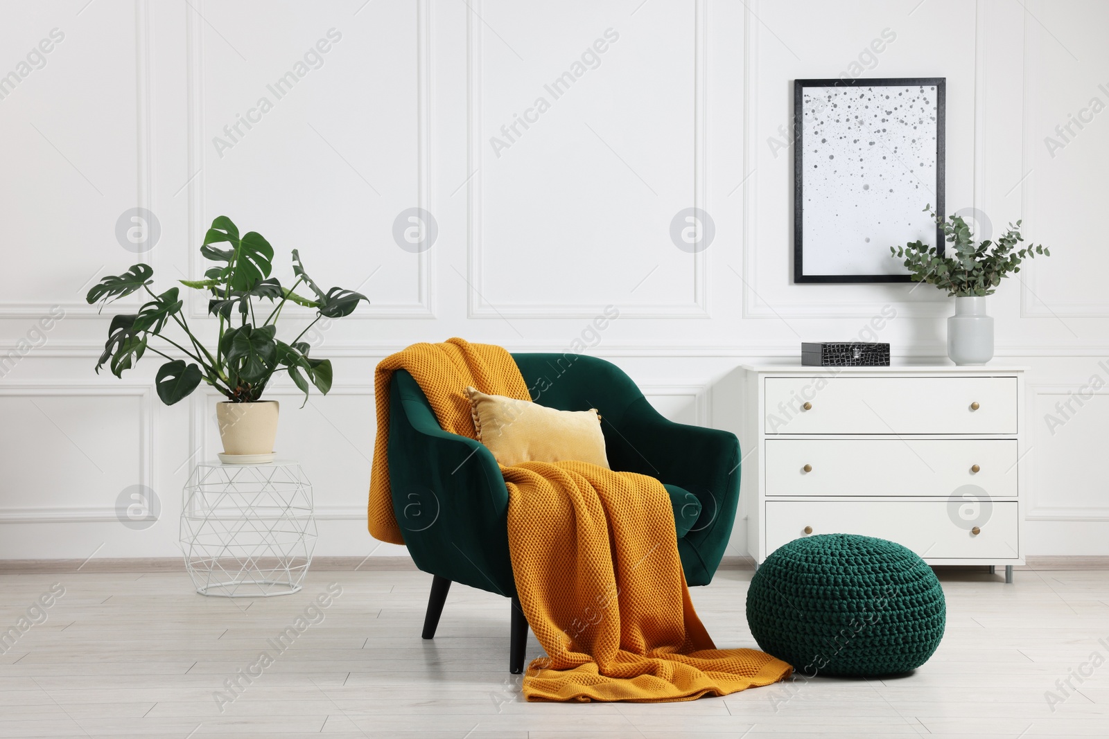 Photo of Comfortable armchair with blanket, ottoman, houseplant and chest of drawers in room