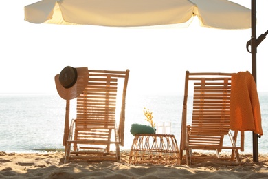 Photo of Wooden deck chairs, outdoor umbrella and beach accessories near sea. Summer vacation