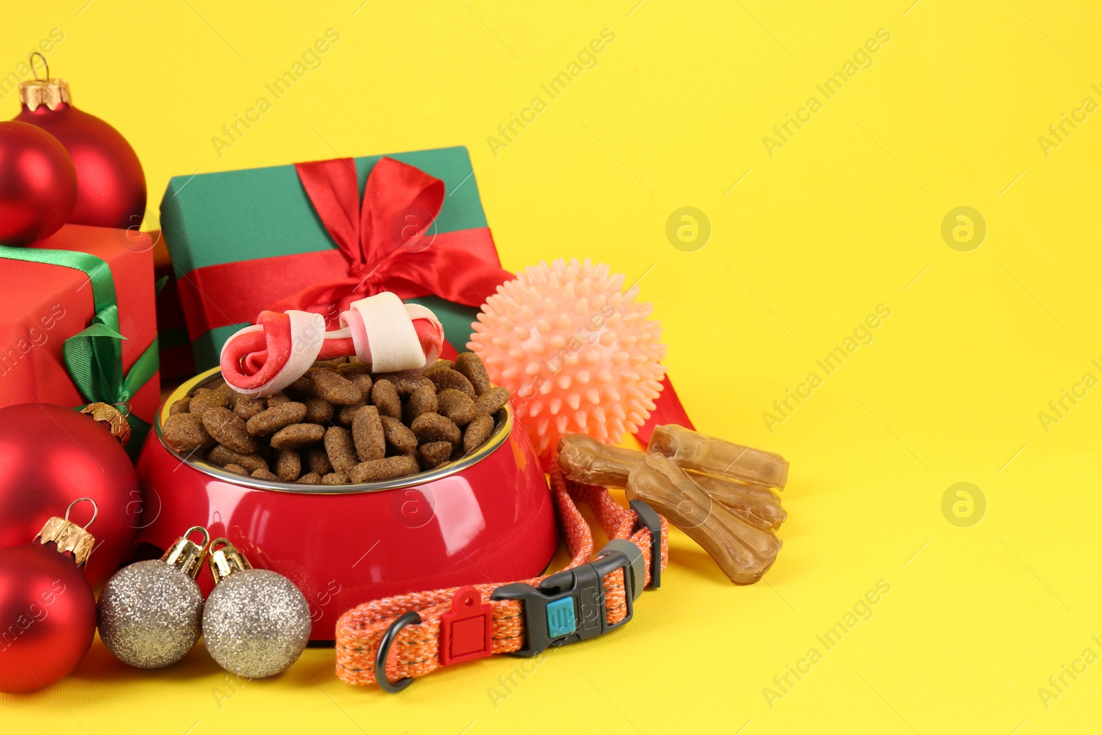 Photo of Different pet goods with Christmas gifts on yellow background, space for text. Shop assortment