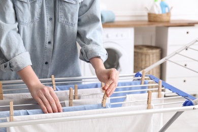 Photo of Woman hanging clean laundry on drying rack in bathroom, closeup
