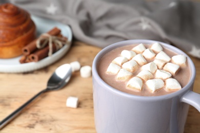 Photo of Delicious hot cocoa drink with marshmallows in cup on wooden table, closeup