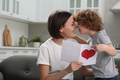 Little son congratulating his mom with Mother`s day at home. Woman holding greeting card