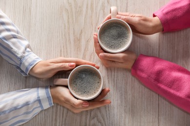 Photo of Women with cups of hot coffee at light wooden table, top view