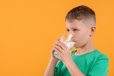 Cute boy drinking fresh milk from glass on orange background, space for text