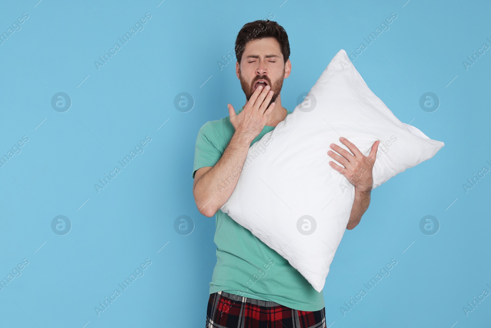 Photo of Tired man with pillow yawns on light blue background, space for text