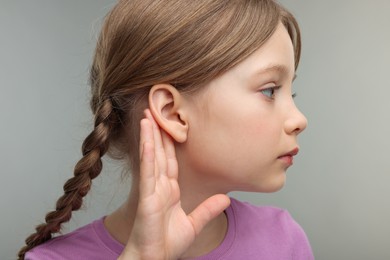 Photo of Little girl with hearing problem on grey background, closeup
