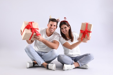 Photo of Beautiful happy couple in Christmas headbands  sitting with gifts on light background